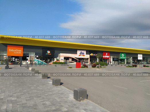 Stop shop shopping center, Sremska Mitrovica, Serbia, June 06, 2022. Square with open shops dm, intersport, dekordom, ccc, lc waikiki. People, parking and pavement. Sunny summer day. Редакционное фото, фотограф Юлия Петровская / Фотобанк Лори