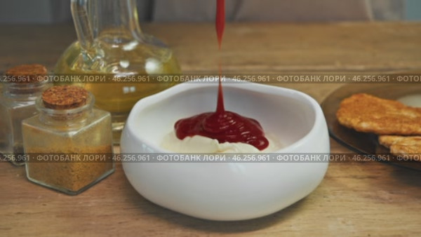 Stream of tomato paste pours into bowl of sour cream. Seasonings are arranged on the table, adding flavor to sauce. Close up. High angle. Стоковое видео, видеограф Strunov David / Фотобанк Лори