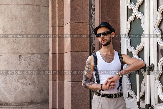 Stylish Individual Leans Against an Ornate Wall Showcasing a Confident Attitude in Urban Setting. Стоковое фото, фотограф Aleksandr Golubev / Фотобанк Лори