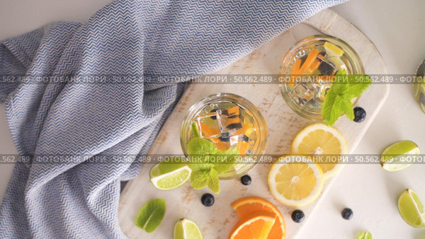 Summer healthy cocktails of citrus infused waters, lemonades or mojitos, with lime lemon orange blueberries and mint, diet detox beverages, in glasses on light background. Стоковое фото, агентство Ingram Publishing / Фотобанк Лори