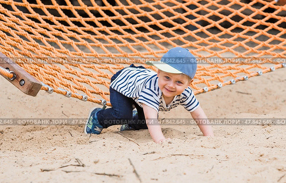 Summer lifestyle. A cute little boy is having fun playing in a hammock on the beach on a modern playground. The concept of family entertainment and leisure. Стоковое фото, фотограф Photojuli / Фотобанк Лори