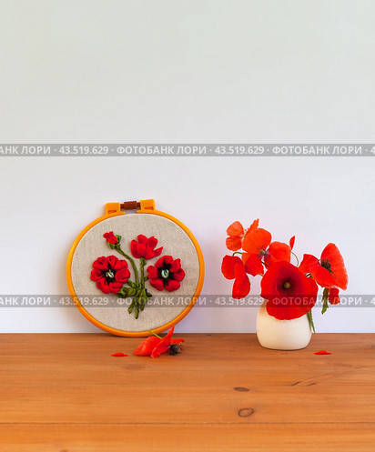 Summer still life with floral handmade embroidery with satin ribbons of red poppy flowers in hoops and bouquet of fresh poppies in a vase on wooden table. Crafts and embroidery as a hobby and leisure. Стоковое фото, фотограф Виктория Катьянова / Фотобанк Лори