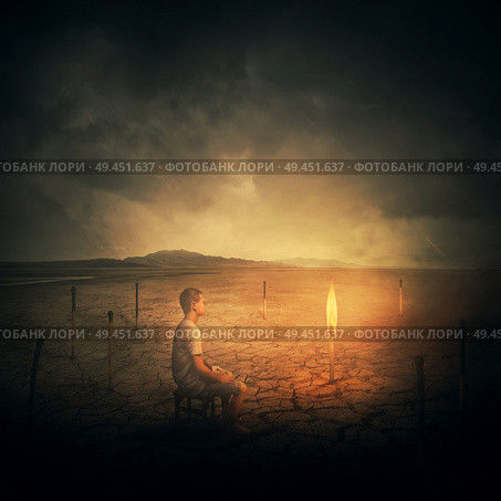 Surrealist concept as a man, sitting on a chair in the middle of a desert, looking at a single burning matchstick through a set of another extinguished, burnt matches. Стоковое фото, агентство Ingram Publishing / Фотобанк Лори