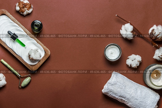 Sustainable beauty setting with eco-friendly products: reusable cosmetic pads, jade massage roller, pipette with facial serum, candle, white towel and cotton on brown background. Frame. Top view. Стоковое фото, агентство Ingram Publishing / Фотобанк Лори