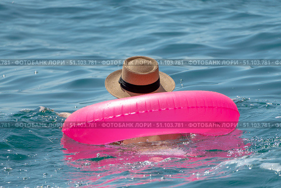 Swimmer, Floating, Ocean: Person relaxing with bright pink inflatable ring and straw hat in calm blue sea on summer day. Стоковое фото, фотограф svetograph / Фотобанк Лори