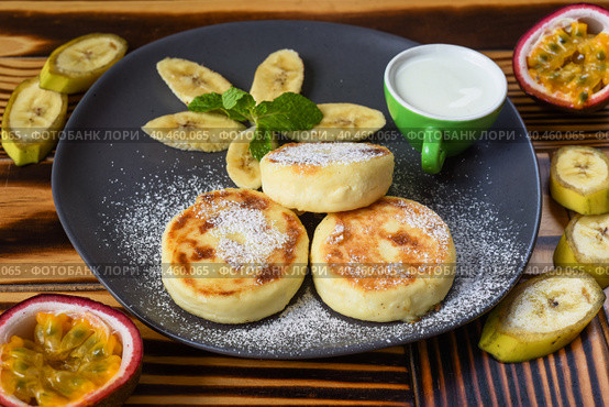 Syrniki or cheese pancakes with cream sauce and bananas on a plate on wooden table close up. Стоковое фото, фотограф Татьяна Терехина / Фотобанк Лори