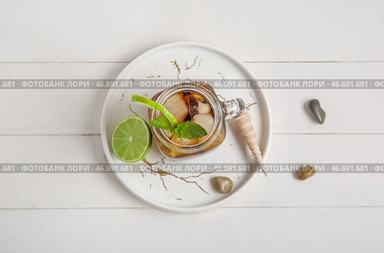 Тарелка с банкой холодного коктейля Cuba Libre, камнями и ракушкой на белом деревянном фоне. Стоковое фото, фотограф Pixel_shot / Фотобанк Лори