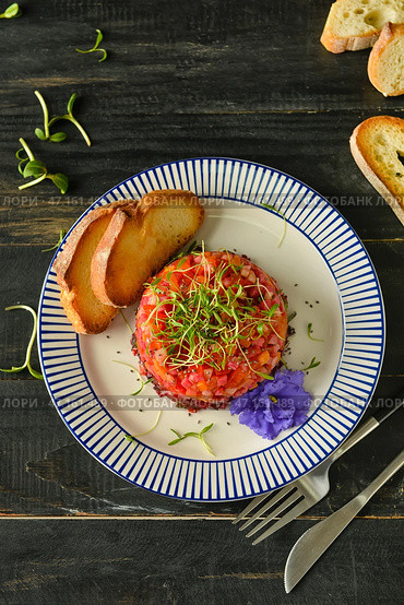 Тарелка с вкусным салатом тартар, поджаренным хлебом и цветами на темном деревянном фоне. Стоковое фото, фотограф Pixel_shot / Фотобанк Лори