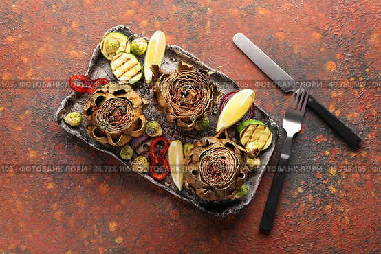Тарелка с вкусными запеченными артишоками и овощами на столе. Стоковое фото, фотограф Pixel_shot / Фотобанк Лори