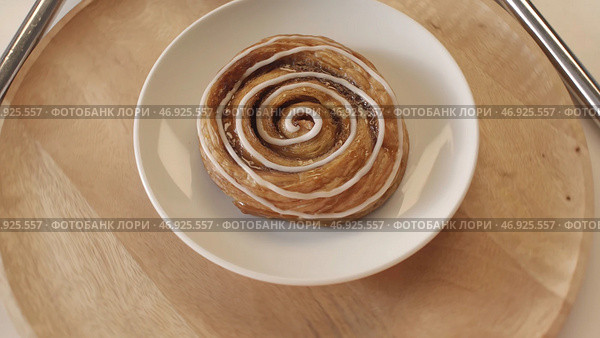 Tasty sweet puff rolls with honey and white glaze lying on the white plate and rotating on the wooden round board. Стоковое фото, фотограф David Kashakhi / Фотобанк Лори