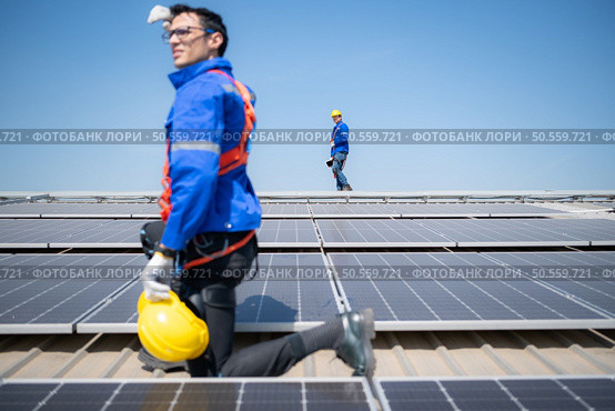Technician repairing solar panels take off his hat and rest in the scorching sun on a factory roof covered with solar panels to receive solar energy. Стоковое фото, агентство Ingram Publishing / Фотобанк Лори