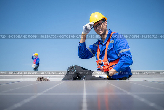 Technician repairing solar panels take off his hat and rest in the scorching sun on a factory roof covered with solar panels to receive solar energy. Стоковое фото, агентство Ingram Publishing / Фотобанк Лори