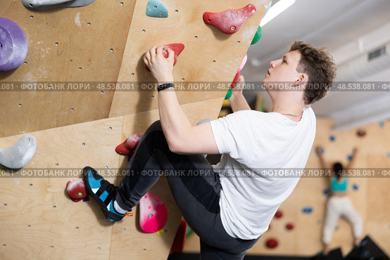 Teenage boy climbs steep artificial wall in sports complex and trains endurance. Стоковое фото, фотограф Яков Филимонов / Фотобанк Лори