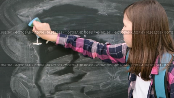 Teenage student girl in shirt with blue backpack writing with chalk numbers and letters on black chalkboard background. Education, back to school and people concept. Joyful Teen girl near blackboard. Стоковое видео, видеограф Марина Демидюк / Фотобанк Лори