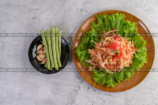 Thai papaya salad on salad in a wooden plate with Yardlong beans and garlic, Top view. Стоковое фото, агентство Ingram Publishing / Фотобанк Лори