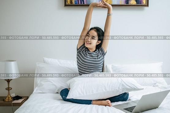 That woman sat on the bed, raised her hand, and placed the laptop. Стоковое фото, агентство Ingram Publishing / Фотобанк Лори