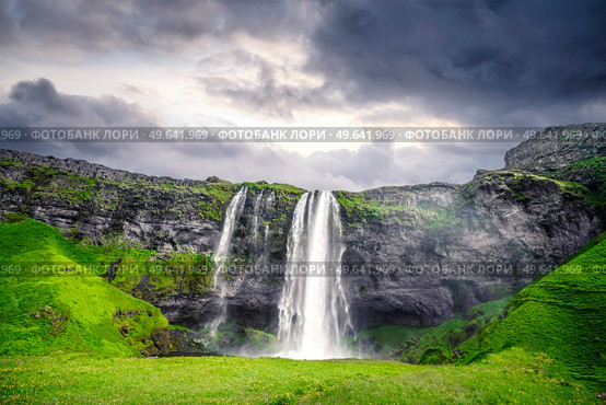 The beautiful Seljalandsfoss waterfall in Iceland surrounded by lava cliffs and green fields in a cloudy sunset. Стоковое фото, агентство Ingram Publishing / Фотобанк Лори