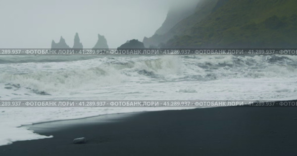 The black sand beach of Reynisfjara with waves hitting the shore on foggy rainy stormy day Vik, Icel. Стоковое видео, видеограф Igor Tichonow / Фотобанк Лори