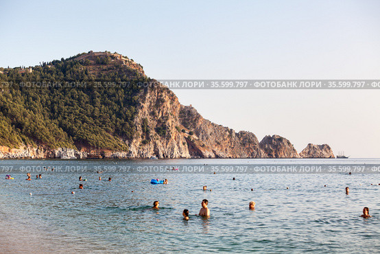 The Kleopatra beach during Covid-19 pandemic. Vacationers sunbathe and swim at resort season. It is popular sandy beach close to mountain with the Alanya castle. Alanya, Turkey (2020 год). Редакционное фото, фотограф Кекяляйнен Андрей / Фотобанк Лори