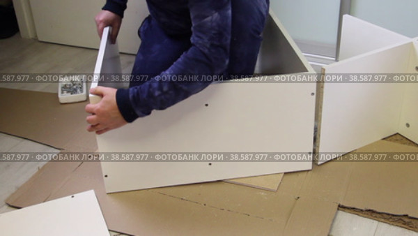 The man connects the side panel and the cover with a Euro screw. Wooden modular rack. Assembling a modular rack. Overall plan. Стоковое видео, видеограф Vadzim Yakubovich / Фотобанк Лори