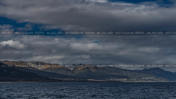 The picturesque mountain range of the Andes. Snow-capped peaks against a background of blue sky and clouds. Ripples on the ocean surface. Argentina. Tierra del Fuego Archipelago. The Beagle channel. Стоковое фото, фотограф Вера Ивановна Кубарева / Фотобанк Лори