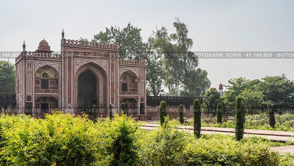 The red sandstone building in the complex of the tomb of Itmad-Ud-Daulah. Arched entrance, white decorative ornaments on the walls. Green vegetation around. India. Agra (2022 год). Стоковое фото, фотограф Вера Ивановна Кубарева / Фотобанк Лори