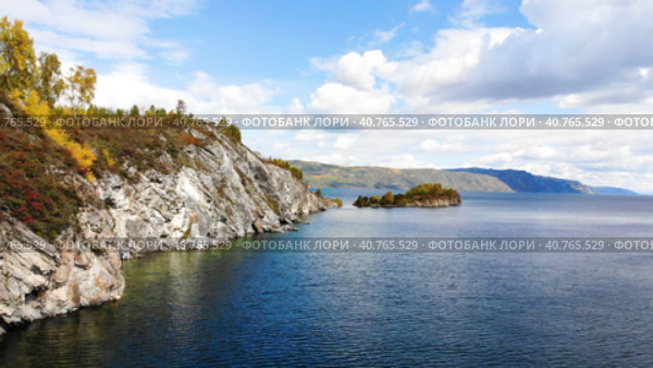 The rocky shore of Lake Baikal in autumn. Flying over the water to the Shaman Cape. Clear water, trees with bright yellow leaves. Скалистый берег озера Байкал осенью. Полет над водой к Шаманскому мысу. Прозрачная вода, деревья с ярко-желтыми листьями. Стоковое видео, видеограф Виктория Тельминова / Фотобанк Лори