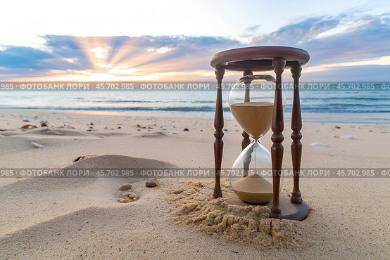 The sun above the horizon and an old beautiful hourglass on the seashore as a symbol of the transience of time. Стоковое AI-изображение, AI-художник Сергей Комаров / Фотобанк Лори