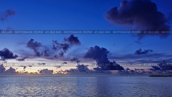 The sun disappeared over the horizon. In the evening sky, orange illumination and purple cumulus clouds. Reflection on the ocean surface. Maldives. Стоковое фото, фотограф Вера Ивановна Кубарева / Фотобанк Лори