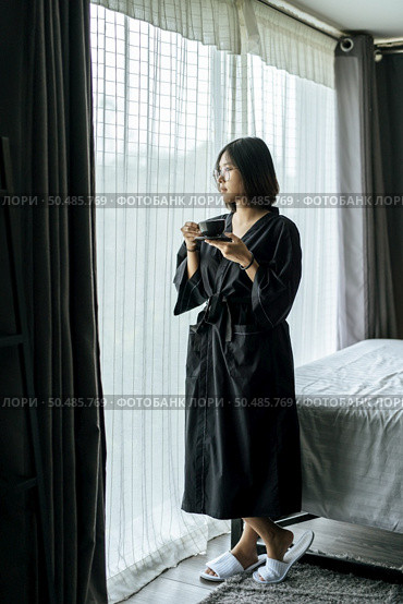 The woman wore a black robe near the window and drank coffee in the bedroom. Стоковое фото, агентство Ingram Publishing / Фотобанк Лори