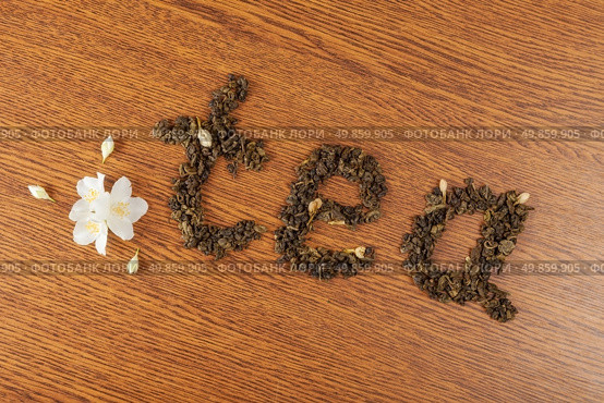 the word "tea" from leaves of green tea on a wooden surface near jasmine flowers. Стоковое фото, агентство Ingram Publishing / Фотобанк Лори