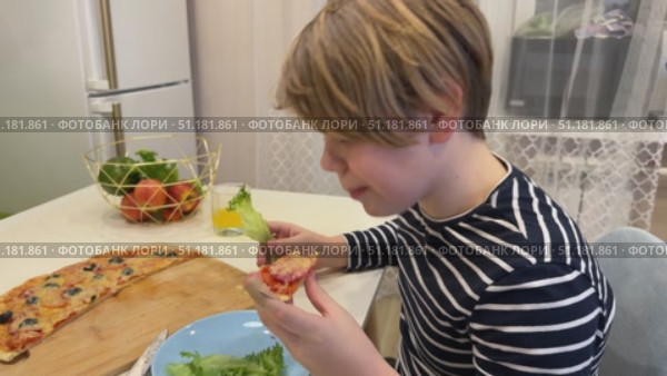 The young boy is munching on pizza in the kitchen, his eyes bright with excitement as he takes another big bite. Стоковое видео, видеограф Ирина Старикова / Фотобанк Лори
