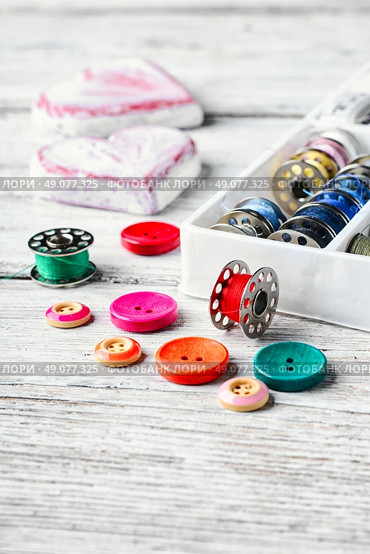 Threads and a set of buttons and bobbin on a bright light background. Working inventory seamstresses. Стоковое фото, агентство Ingram Publishing / Фотобанк Лори