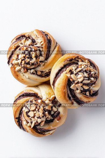 Three freshly baked chocolate swirl buns topped with chopped almonds, arranged on a white background, showcasing a delicious combination of texture, sweetness, and detail. Стоковое AI-изображение, AI-художник Катерина Бондарец / Фотобанк Лори