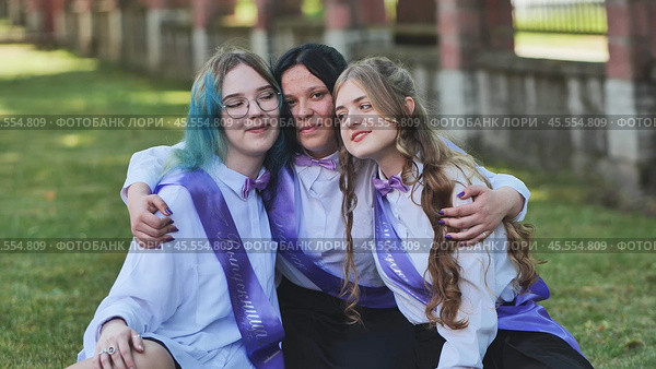 Three happy graduates in sashes share a heartfelt goodbye on their last day of school, celebrating academic success with joy and excitement. Стоковое фото, фотограф Mikhail Davidovich / Фотобанк Лори