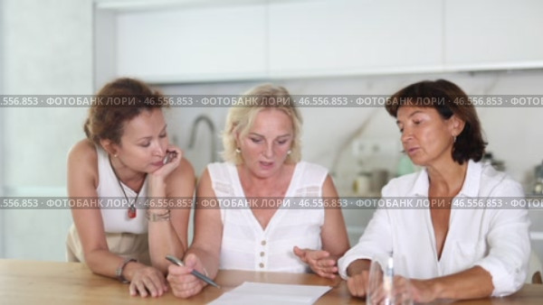 Three women help each other sort out financial documents in the kitchen of a home. Стоковое видео, видеограф Яков Филимонов / Фотобанк Лори