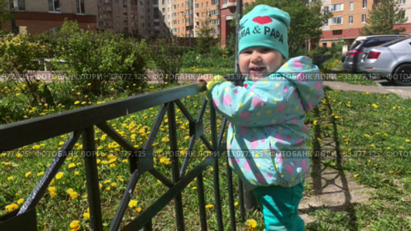 Toddler girl holds the rails while standing on urban courtyard of apartment house or condominium. Стоковое видео, видеограф Кекяляйнен Андрей / Фотобанк Лори