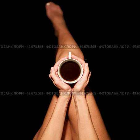 Top view of crop unrecognizable barefooted female sitting in black studio with cup of hot coffee. Crop anonymous woman with coffee cup in black studio. Стоковое фото, агентство Ingram Publishing / Фотобанк Лори