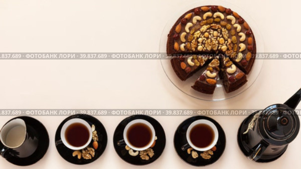 Top view of three cups of black tea, a jug of milk and a teapot next to a festive homemade nutty, chocolate cake on a light table. Culinary cake recipe, free space for text. Flat lay, copy space, mock up. Стоковое видео, видеограф Виктория Катьянова / Фотобанк Лори