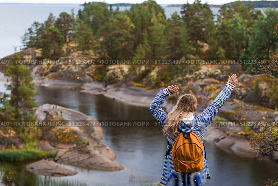 Tourism. Hiking. Ladoga skerries on Lake Ladoga. A female tourist in a raincoat with a backpack on the rocky islands looks into the distance. Republic of Karelia, Russia. Стоковое фото, фотограф Photojuli / Фотобанк Лори