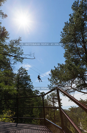 Tourist is going down the ropes - a bungee cable - from a mountain waterfall above the wooded gorge of the Kyngarga River. Fun active summer holiday. Siberia. Buryatia. Arshan resort. Стоковое фото, фотограф Виктория Катьянова / Фотобанк Лори