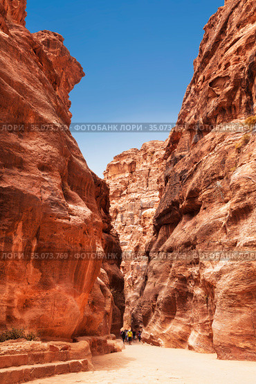 Tourists in narrow passage of rocks of Petra canyon in Jordan. Petra has been a UNESCO World Heritage Site since 1985. Way through Siq gorge to stone city Petra (2012 год). Стоковое фото, фотограф Наталья Волкова / Фотобанк Лори