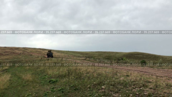 Tractor with hay bales in wagon driving through an agricultural field after harvesting grain crops. Haymaking (2021 год). Редакционное видео, видеограф Кекяляйнен Андрей / Фотобанк Лори