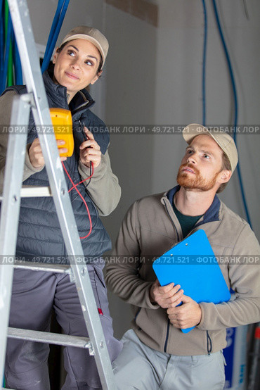 tradesman with female electrician on stepladder. Стоковое фото, агентство Ingram Publishing / Фотобанк Лори