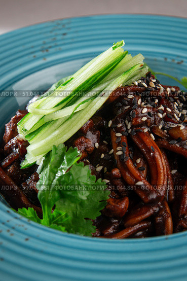 Traditional Korean jajangmyeon noodles with rich black bean sauce, fresh cucumber, sesame seeds and herbs served in a rustic blue ceramic bowl. Стоковое фото, фотограф Aleksandr Gavrilychev / Фотобанк Лори