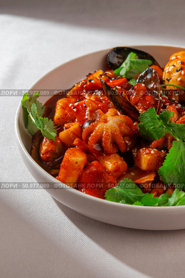 Traditional Korean tteokbokki with seafood mix including mussels, baby octopus, spicy sauce, boiled egg and sesame served in a ceramic bowl under natural daylight. Стоковое фото, фотограф Aleksandr Gavrilychev / Фотобанк Лори