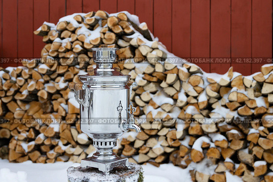 Traditional Russian samovar. A classic metal samovar against the background of a stack of firewood. Tea tradition in a village in Russia. Rural lifestyle. Nostalgic mood. Winter in the countryside. Стоковое фото, фотограф Андрей Степанов / Фотобанк Лори