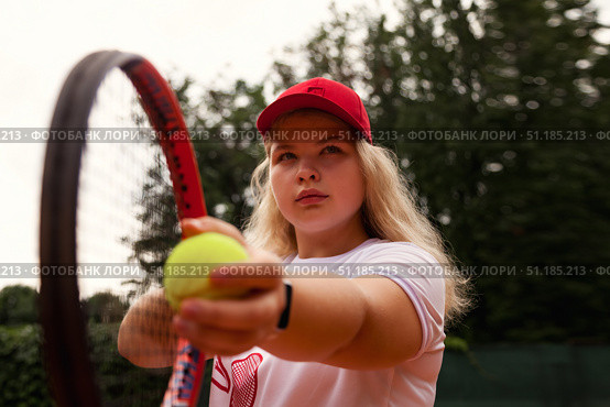 Training Hard at the Tennis Court, a Teenage Girl Prepares to Serve Under the Clear Blue Sky. Стоковое фото, фотограф Aleksandr Golubev / Фотобанк Лори