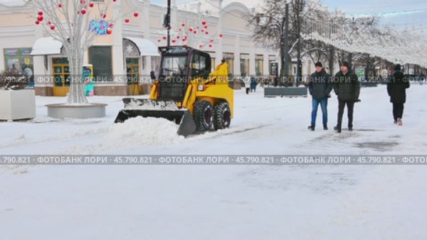 Трактор расчищает от снега оживленную пешеходную улицу в центре города, украшенную к предстоящему Новому году. Редакционное видео, видеограф Александр Бушков / Фотобанк Лори