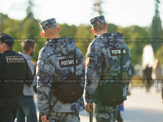 Translation of the text in Russian into English - Police. Police patrol in the public city park of Moscow. Guardsmen. Sunny summer day. Safety and security concepts. Backs, rear view. (2022 год). Редакционное фото, фотограф YuryKara / Фотобанк Лори